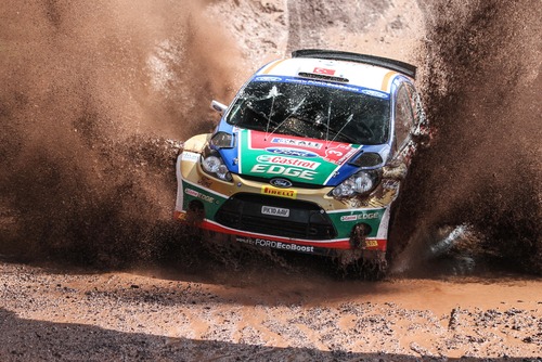 A colorful rally race car comes towards the camera in a spray of dirt