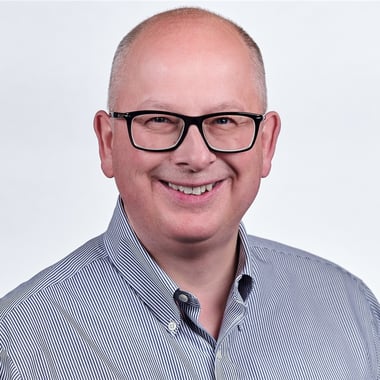 Steve Yemm, a person with very short grey hair and glasses, against a grey-white background